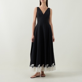 Model wearing Jonathan Simkhai black midi dress with deep V-neck, full skirt, and white floral lace hem trim, styled with tan strappy sandals.