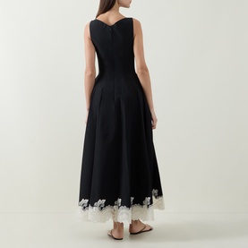 Model wearing Jonathan Simkhai black multi dress, back view, sleeveless with pleated skirt and white lace hem trim, styled with tan sandals.