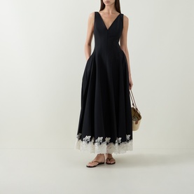 Model wearing Jonathan Simkhai black midi dress with V-neckline, full skirt and white lace hem trim, styled with tan sandals and woven bag.