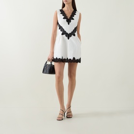 Model wearing Jonathan Simkhai Ivory Multi mini dress with black lace trim, styled with a black top-handle bag and nude strappy heels.