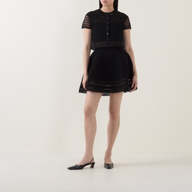 Model wearing Jonathan Simkhai black merino wool short-sleeve knit top with sheer stripe detail, styled with matching mini skirt and black slingback