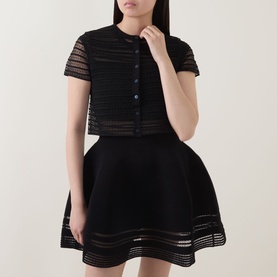 Model wearing Jonathan Simkhai black sheer stripe merino wool crop top with short sleeves, styled with matching black flared mini skirt.