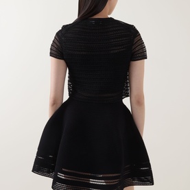 Model wearing Jonathan Simkhai black merino wool striped mini dress with flared skirt, sheer stripe panels, and short sleeves, rear view.