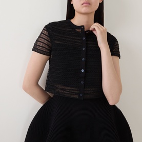 Model wearing Jonathan Simkhai black sheer stripe merino wool cropped top with short sleeves and button front, styled with black full skirt.