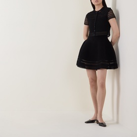 Model wearing Jonathan Simkhai black merino wool short-sleeve knit top with sheer stripe detail, styled with matching black mini skirt and black