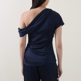Model wearing Jonathan Simkhai top in midnight, asymmetric one-shoulder drape design, shown from back, styled with navy trousers.