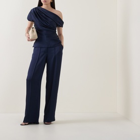 Model wearing Jonathan Simkhai midnight navy one-shoulder draped acetate top, styled with wide-leg trousers and cream clutch bag.