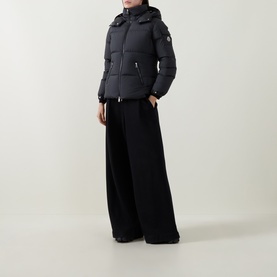 Model wearing Moncler black hooded puffer jacket with logo badge, styled with wide-leg black trousers.