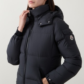 Model wearing Moncler black padded down jacket with detachable hood, zip fastening, and arm logo badge.