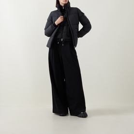 Model wearing Moncler black padded jacket with high neck, styled with wide-leg black trousers and black shoes.