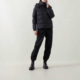 Model wearing Moncler black hooded puffer jacket with quilted panels, styled with black joggers and black chunky sole ankle boots