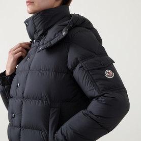 Model wearing Moncler black quilted down jacket with high collar, hood, and logo badge on sleeve