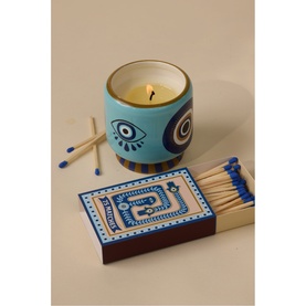 Paddywax A Dopo Eye Ceramic Candle in blue evil eye-painted vessel, styled with a decorative matchbox and loose matches.