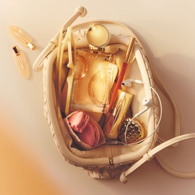 Estee Lauder EDP gold bottle in an open cream leather bag with lipstick, earbuds, and accessories
