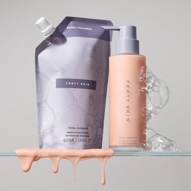Fenty Skin Total Cleanse cleanser bottle and refill pouch with peach-toned product drips on grey surface