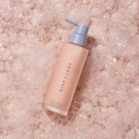 Fenty Skin cleanser in peach-toned pump bottle, shown on rose-tinted textured surface
