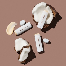 Fenty Skin lip care sticks displayed with coconut halves and cream texture on a warm brown background