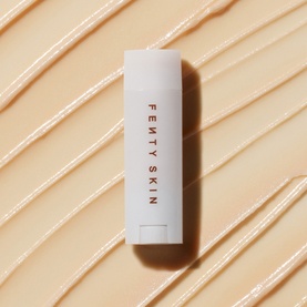 Fenty Skin lip care stick in white packaging, shown upright against a creamy textured swatch background