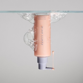 Fenty Skin cleanser in peach pump bottle submerged in water with bubbles, highlighting its water-activated formula