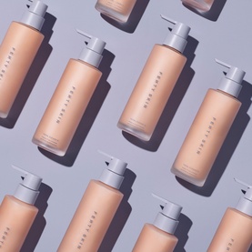 Fenty Skin cleanser in peach pump bottles arranged in a repeating flat-lay pattern on a lilac background