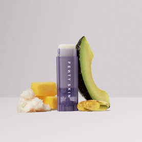 Fenty Skin lip care stick in purple packaging, styled with avocado, shea butter, and oil drop ingredients