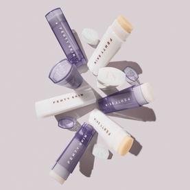 Fenty Skin lip balm sticks in white and lavender packaging, shown open and closed, arranged in a flat lay group shot