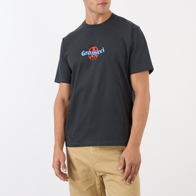 Model wearing Gramicci Ladybug Logo T-Shirt in black with ladybug chest graphic, styled with beige chinos.