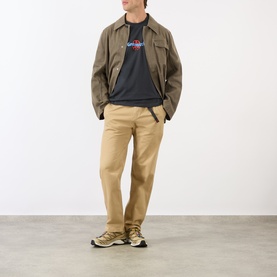 Model wearing Gramicci Ladybug Logo T-Shirt in black with khaki trousers, olive jacket, and gold-tone trainers.