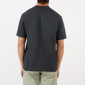 Model wearing Gramicci One Point Chest Pocket T-Shirt in black, rear view, crew neck, short sleeves, styled with light khaki trousers.