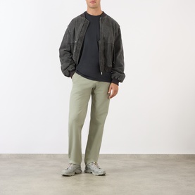 Model wearing Gramicci One Point Chest Pocket T-Shirt in Black, styled with a dark bomber jacket, sage green trousers and grey trainers.