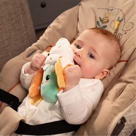 Baby holding Play Easy multi-coloured plush toy featuring white, orange and mint green soft character, while reclining in a baby bouncer chair.