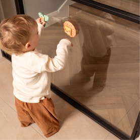 Play Easy multi-coloured toy shown in use, held by a toddler kneeling by a glass panel, with a second piece visible on the surface.