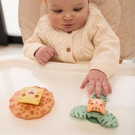 Baby in high chair reaching for Play Easy multi-coloured lion and leaf-shaped teething toys on tray
