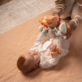 Play Easy multi-coloured sensory toys shown with baby lying on peach play mat, adult holding soft activity toy above infant