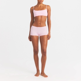 Model wearing Skims pink bralette with matching pink boy shorts