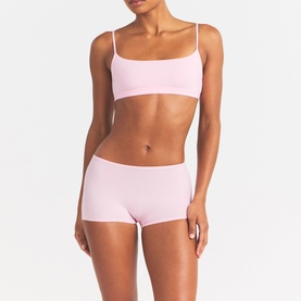 Model wearing Skims pink bralette with thin straps, styled with matching pink boy shorts.
