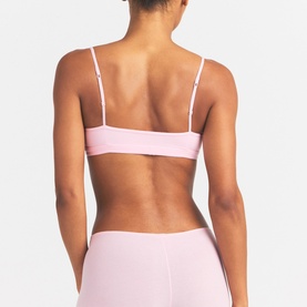 Model wearing Skims pink bralette, back view, with thin adjustable straps, styled with matching pink leggings