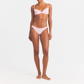 Model wearing Skims pink underwire bralette and matching low-rise bikini briefs, full-body front view