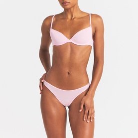 Model wearing Skims pink underwired bra with thin straps, styled with matching pink bikini-style briefs with side tie detail