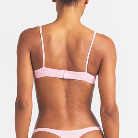 Model wearing Skims pink bra, rear view showing adjustable back closure and matching briefs.