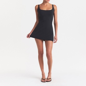 Model wearing Skims black mini dress with square neckline and thin straps, styled with tan strappy sandals