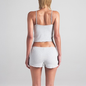 Model wearing Skims light heather grey pyjama cami top and shorts set, shown from the back with lettuce-edge hem detailing.