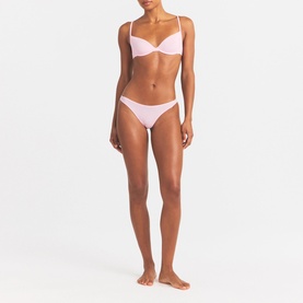 Model wearing Skims pink thong brief with matching pink underwired bralette