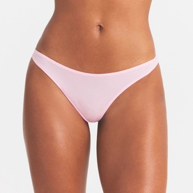Model wearing Skims pink thong brief, smooth seamless fabric, minimal coverage with high-cut leg