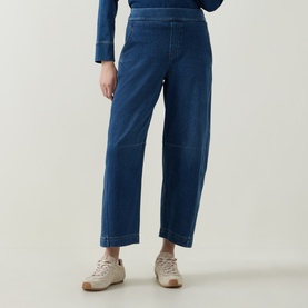 Model wearing Spanx Denim Barrel Leg Track Pants in dark blue, high-rise cropped barrel leg, styled with cream trainers and blue long-sleeve top