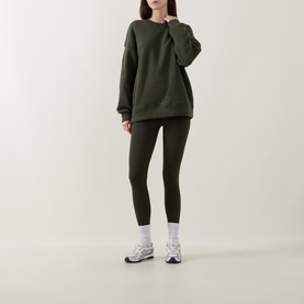 Model wearing dark olive green oversized crew neck sweatshirt and matching leggings, styled with white socks and grey trainers