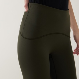 Model wearing olive green high-waist leggings with side pocket detail, paired with a black top