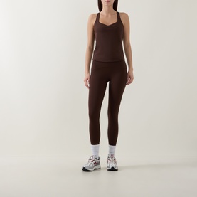 Model wearing dark brown racerback sports top and matching high-waist leggings, styled with white ankle socks and chunky trainers.