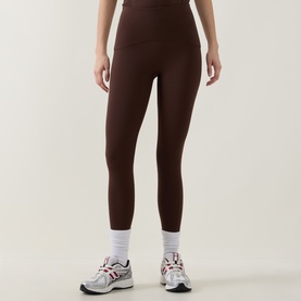 Model wearing dark brown high-waist leggings, styled with white ankle socks and grey and white trainers