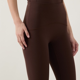 Model wearing dark brown high-waisted leggings with wide waistband, close-up view of hip and thigh area